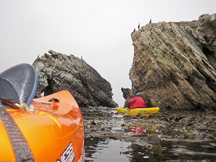 kayakers paddle around diagonally striated rock formations